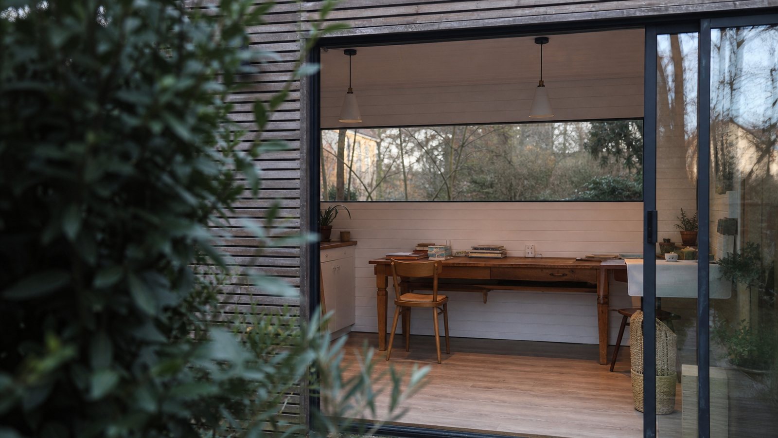 Studio de jardin chaleureux occupé en hiver, lumière douce et grande baie donnant sur le jardin